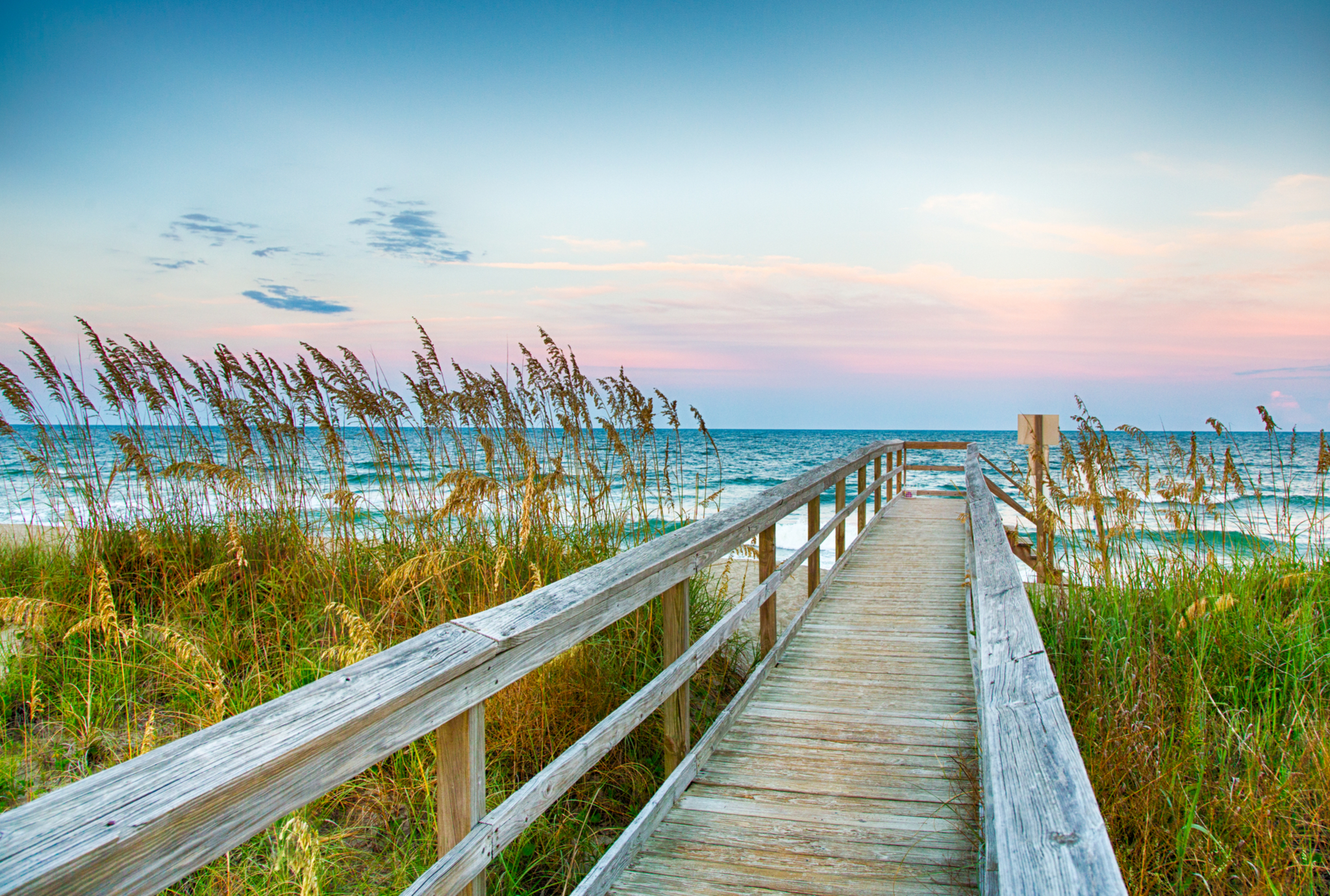 Beautiful sun set with a pink sky looking down a boardwalk to the beach